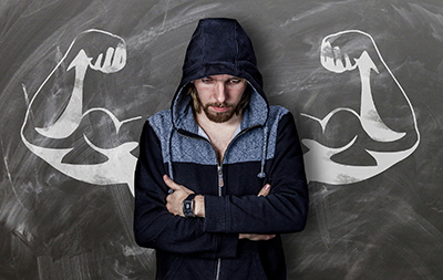 man with arms folded, but flexed muscles drawn on chalkboard behind him