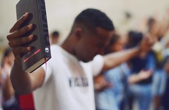 man holding Bible with outstretched hands and praying with