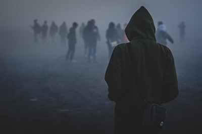 young man in hoodie facing a distant crowd through the fog