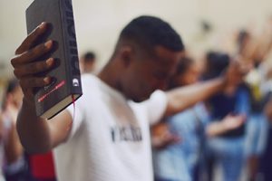 man holding Bible with outstretched hands and praying with 