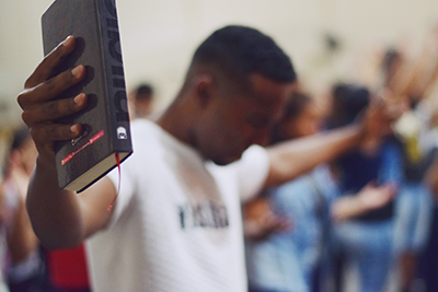 man holding Bible with outstretched hands and praying with