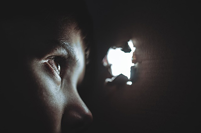 boy in darkness peering through an opening of light