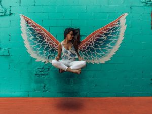 girl appearing to float in front of a pair of wings painted on a wall