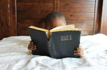 young boy reading Bible in bed