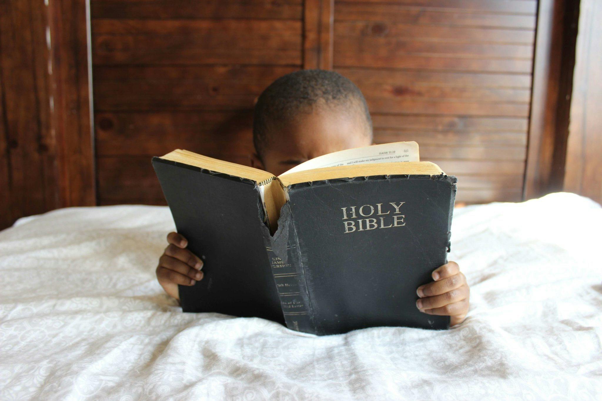 young boy reading Bible in bed