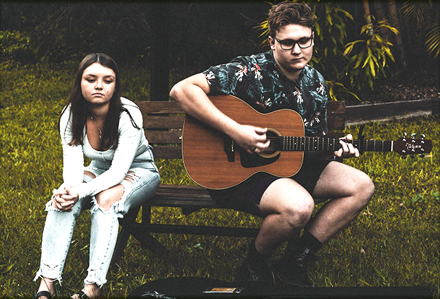 downcast youth, one holding a guitar