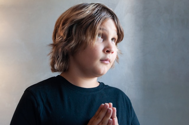 boy in prayer posture looking hesitantly upward